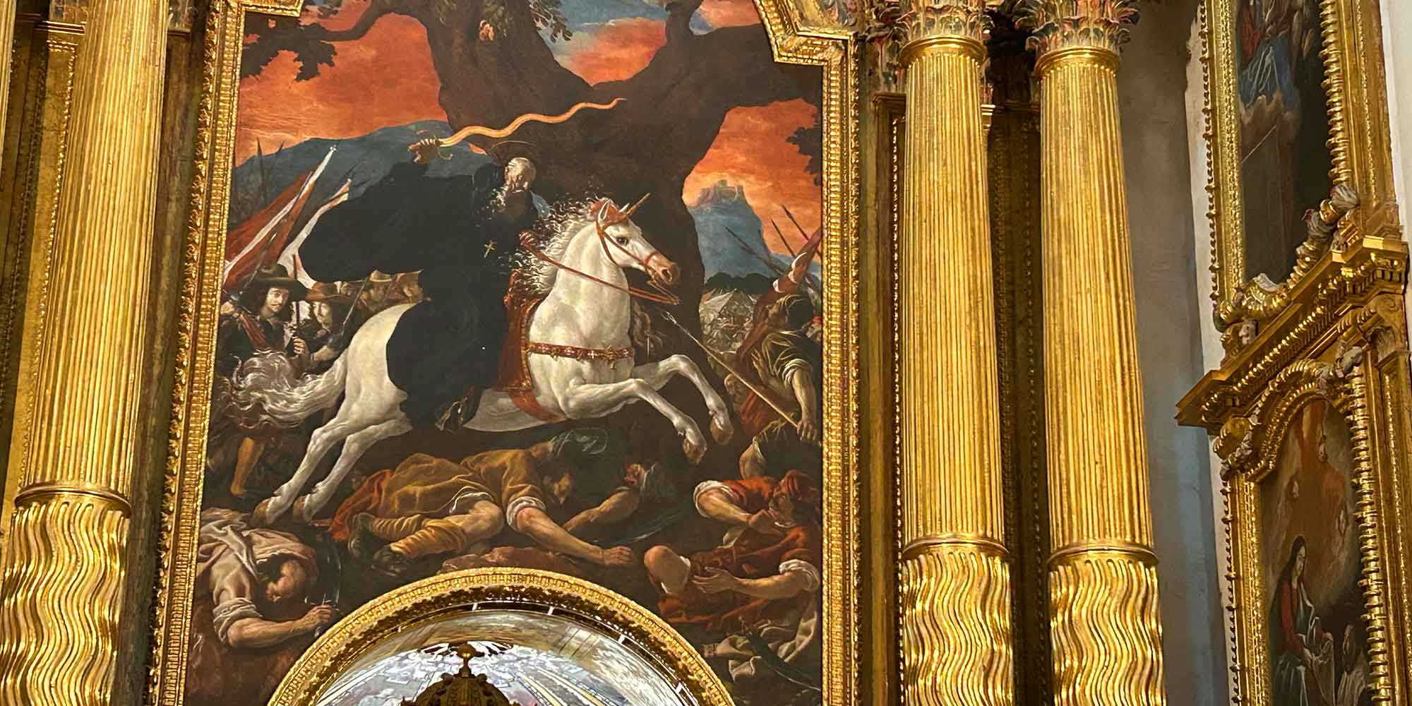 El Monasterio de Yuso alberga uno de los legados cumbre del barroco monástico español gracias a Fray Juan Rizzi (1600-1681), monje benedictino, teólogo y pintor fundamental de la escuela madrileña. Durante su intensa estancia claustral en el valle entre 1653 y 1656, Rizzi renovó la identidad visual del cenobio a través de un extraordinario conjunto de más de veinte lienzos que fusionan el realismo y el tenebrismo naturalista. Desde las monumentales pinturas del Retablo Mayor —presididas por la icónica representación de San Millán en la batalla de Simancas— hasta los detallados ciclos hagiográficos sobre la vida de San Benito y los santos de la Cogolla que hoy custodia el museo, su obra plasma en el lienzo la profunda herencia espiritual y cultural que define a San Millán como Patrimonio de la Humanidad.